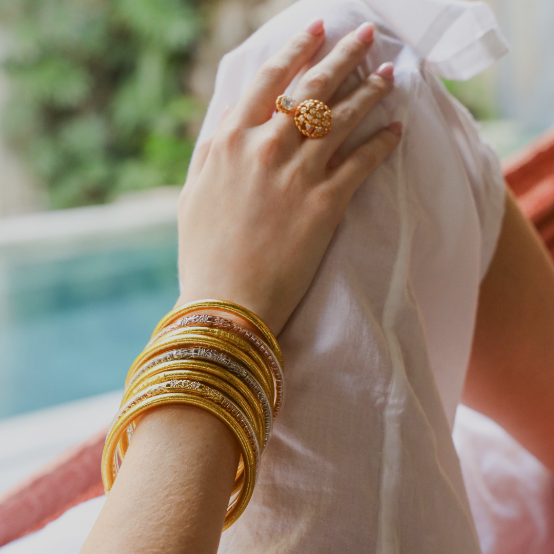 a hand with gold bracelets and a ring on a white shirt