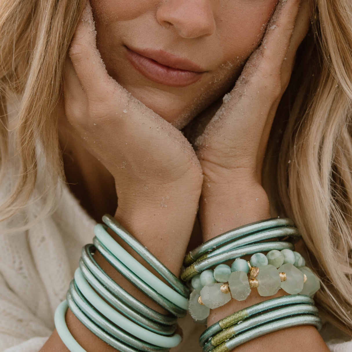 Close-up of a woman's face with hands on cheeks, wearing multiple green bracelets.