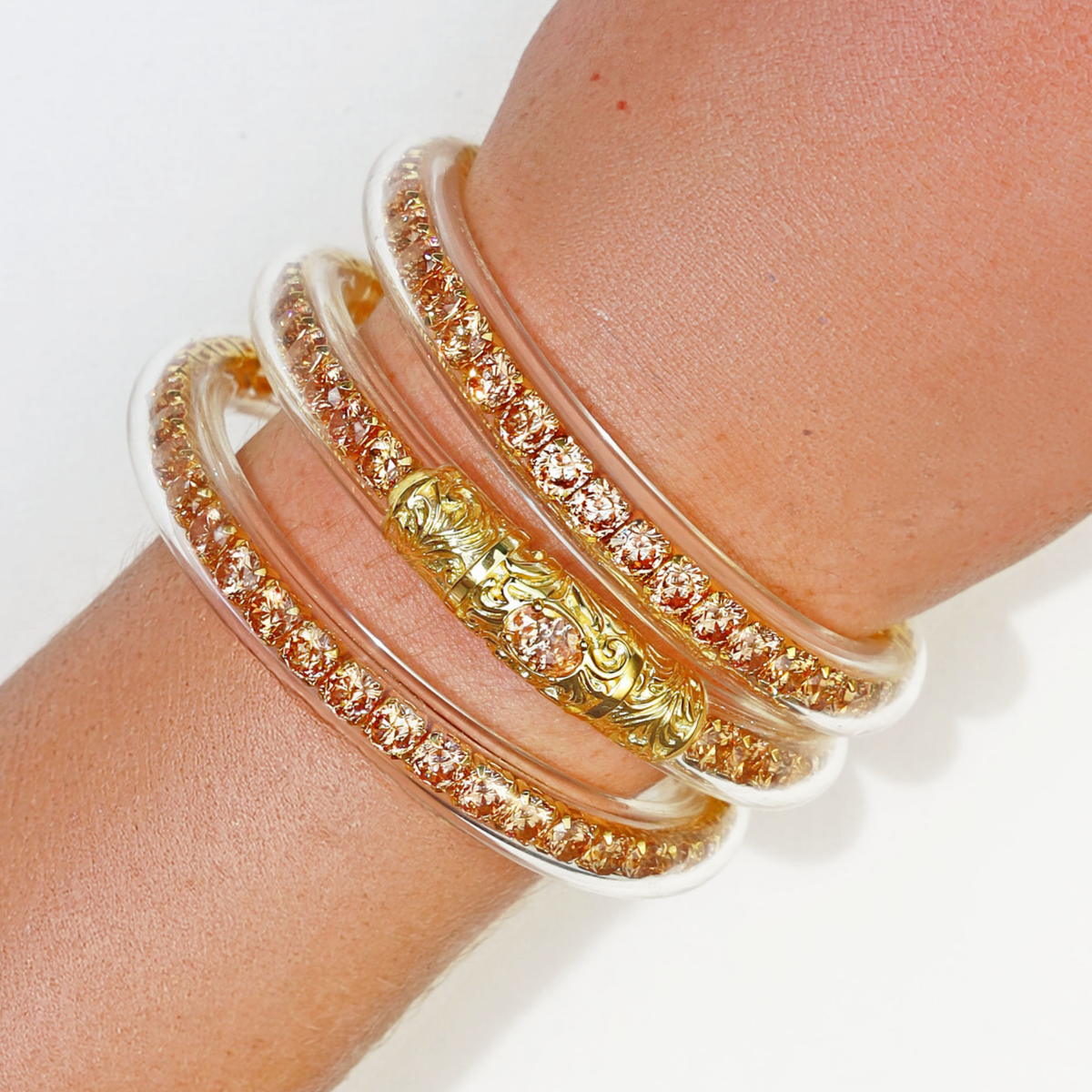BuDhaGirl crystal bangle bracelets for women stacked on a wrist with champagne colored stones and an ornate gold centerpiece