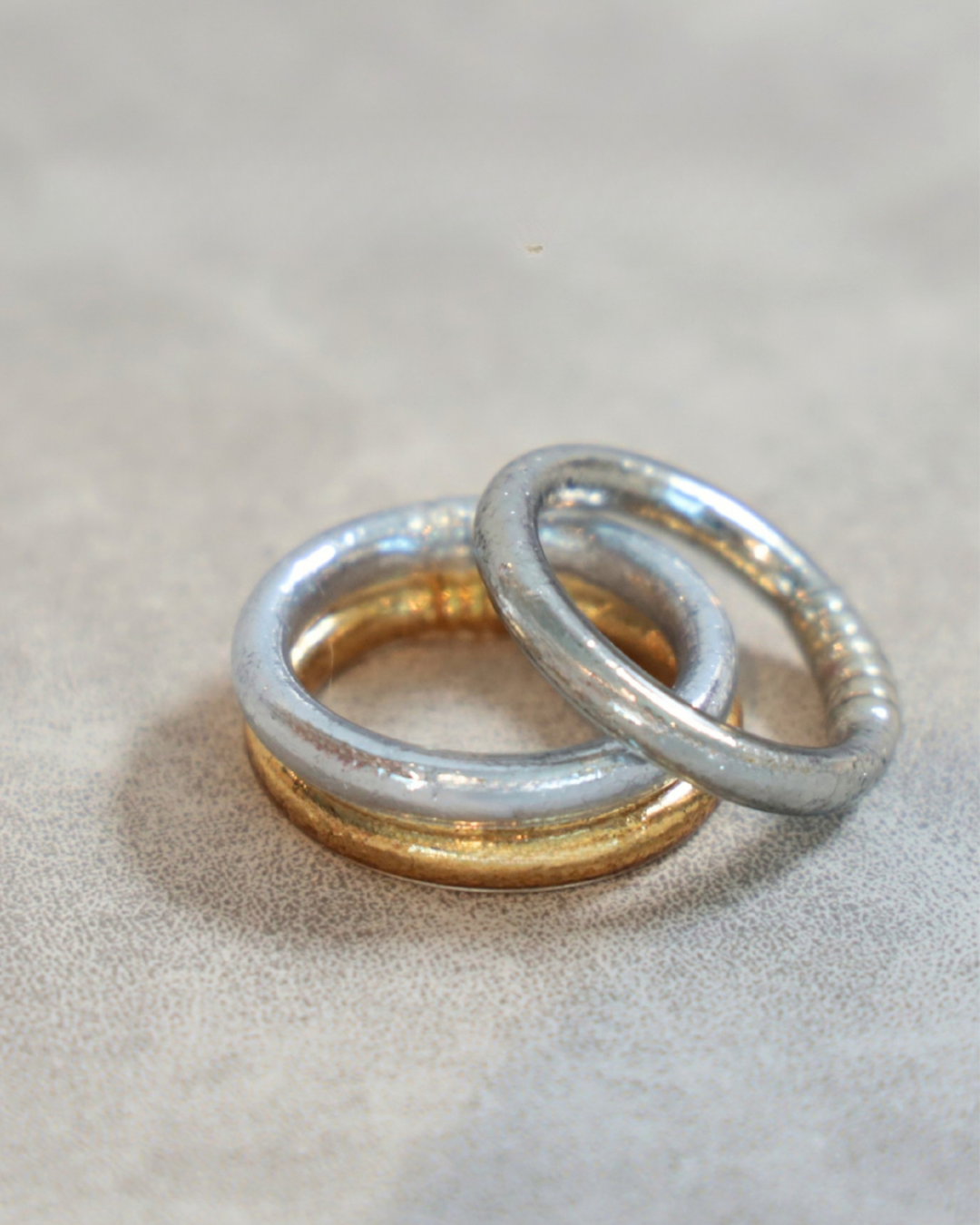 Two interlocking metallic bangle bracelets in silver and gold tones resting on a textured neutral surface