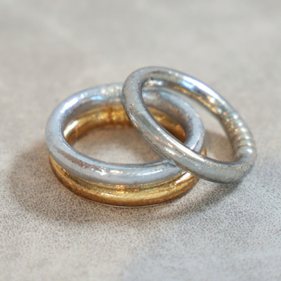 Two interlocking metallic bangles with silver and gold toned finishes resting on a softly textured neutral surface