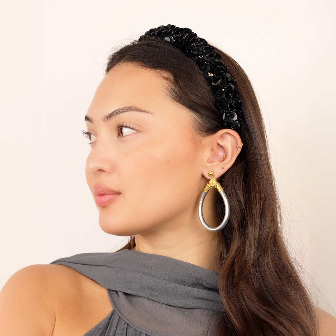 Woman wearing a black beaded headband and gold teardrop earrings on a plain background
