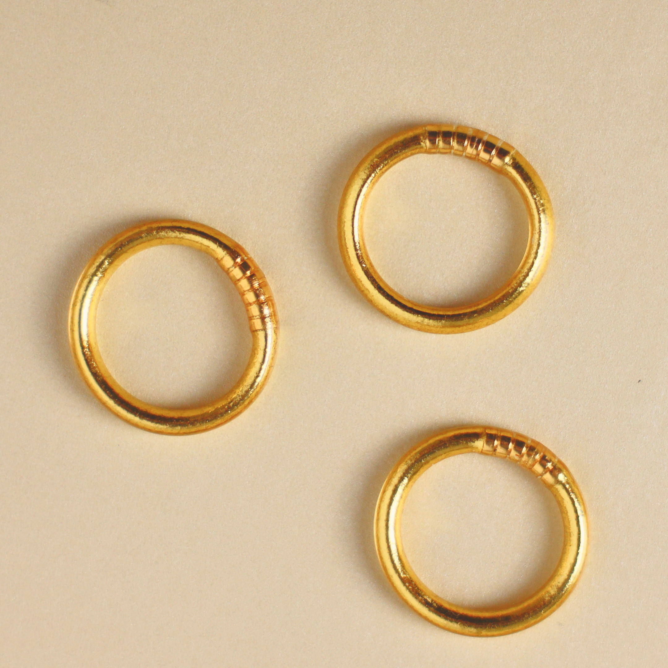Three gold rings with textured edges on a beige background