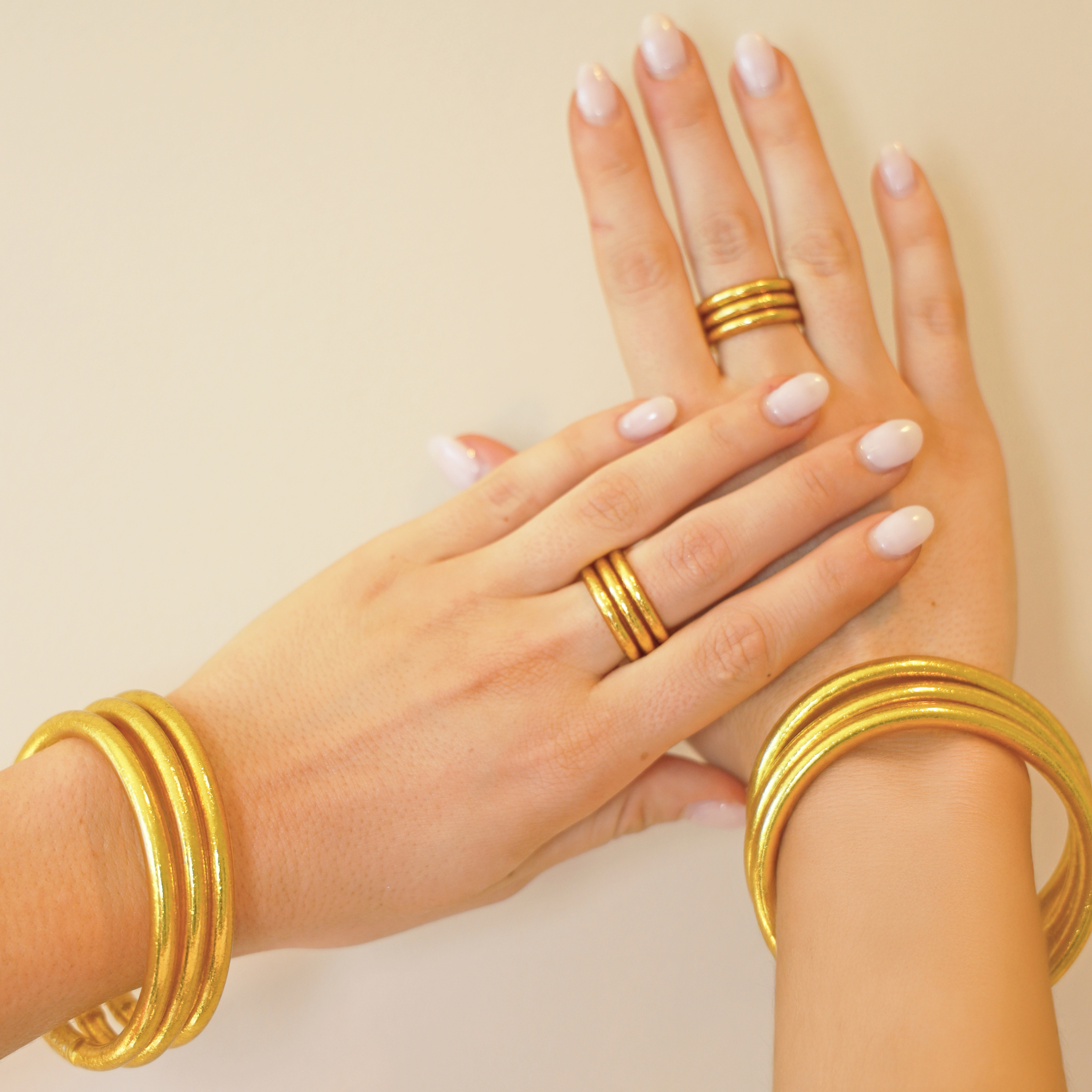 Close-up of a hand with multiple gold rings and bangles on a beige background