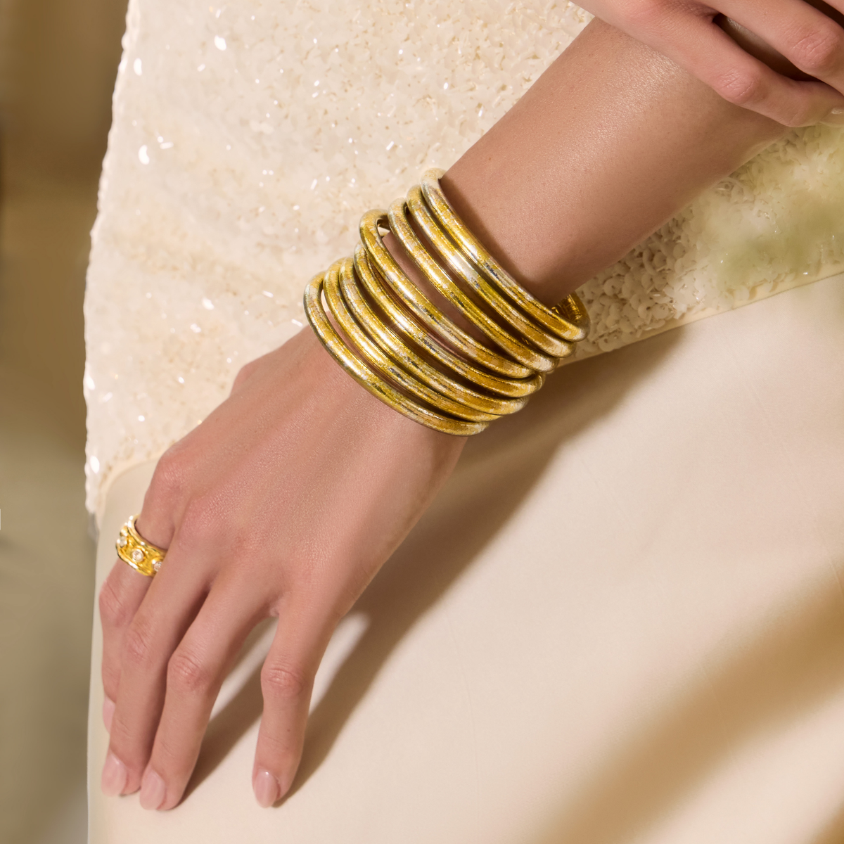 BuDhaGirl gold bangle bracelets for women stacked on a models wrist against a shimmering cream outfit