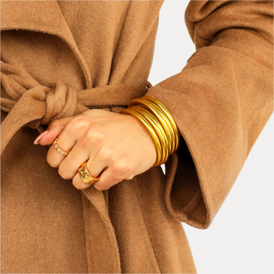 Close-up of a person wearing gold bangles and rings with a brown coat.